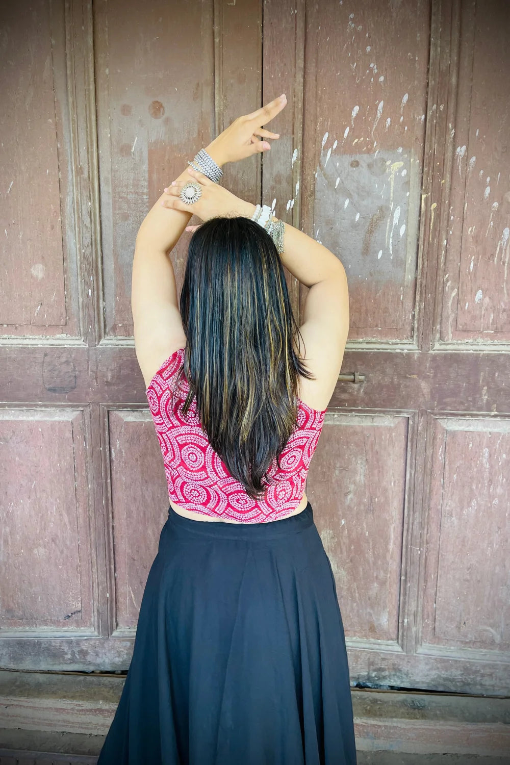 “Woman wearing the Dori cotton westcoat with circular white block print on maroon, cropped sleeveless fit, styled with oxidized silver jewelry, standing before a rustic wooden door”.