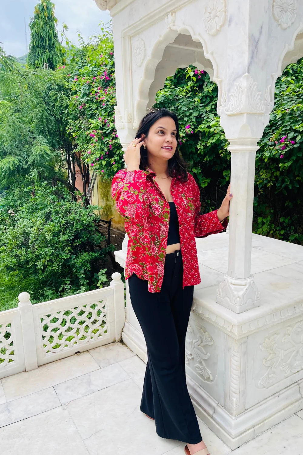 “Woman wearing the Gulzaar cotton shirt in a red floral print, relaxed fit, button‑down, in an outdoor garden setting.”