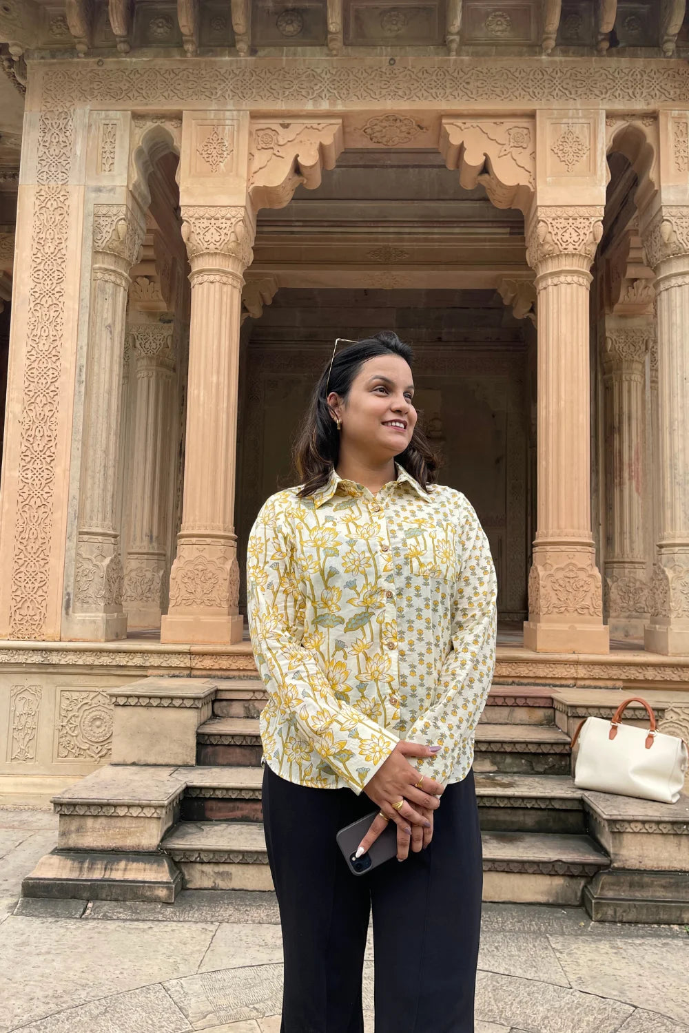 “Woman wearing the Lotus cotton shirt in a light yellow floral print, relaxed fit, button‑down, standing in front of carved sandstone pillars”.