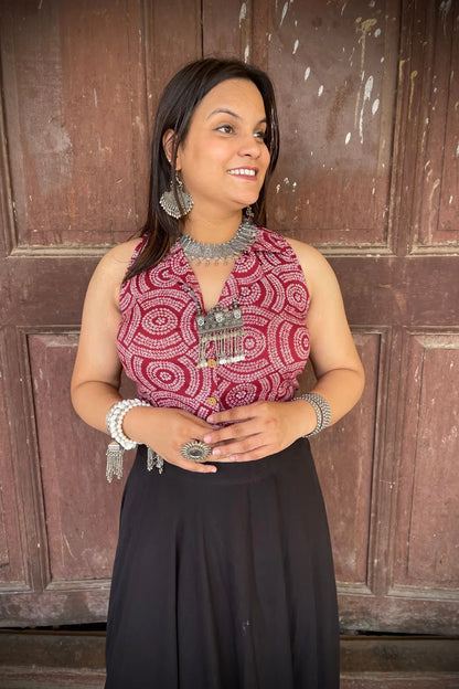 “Woman wearing the Dori cotton westcoat with circular white block print on maroon, cropped sleeveless fit, styled with oxidized silver jewelry, standing before a rustic wooden door”.