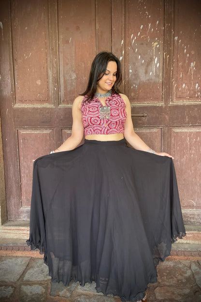 “Woman wearing the Dori cotton westcoat with circular white block print on maroon, cropped sleeveless fit, styled with oxidized silver jewelry, standing before a rustic wooden door”.