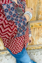 “Woman wearing the Mahreen cotton shirt with maroon chevron print and contrast floral patch pockets/cuffs, relaxed fit, button‑down, standing before a carved wooden door”.