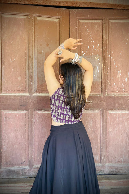 “Woman wearing the Ojal cotton westcoat in plum with gold block print, cropped sleeveless fit, styled with oxidized silver jewelry, standing before a rustic wooden door”.