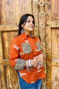 “Woman wearing the Panchi cotton shirt in rust with bird block motifs and contrast paisley patches, relaxed fit, button‑down, standing before a carved wooden door”.